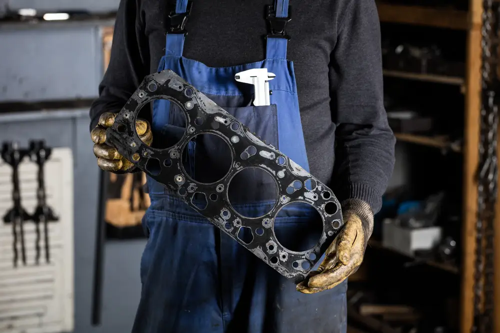 Car mechanic in garage with old engine head gasket